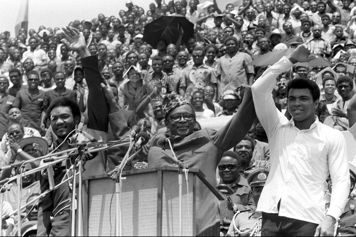 File photo of Zaire’s President Mobutu Sese Seko (center) as he raises the arms of heavyweight champ George Foreman )left) and Muhammad Ali (right)