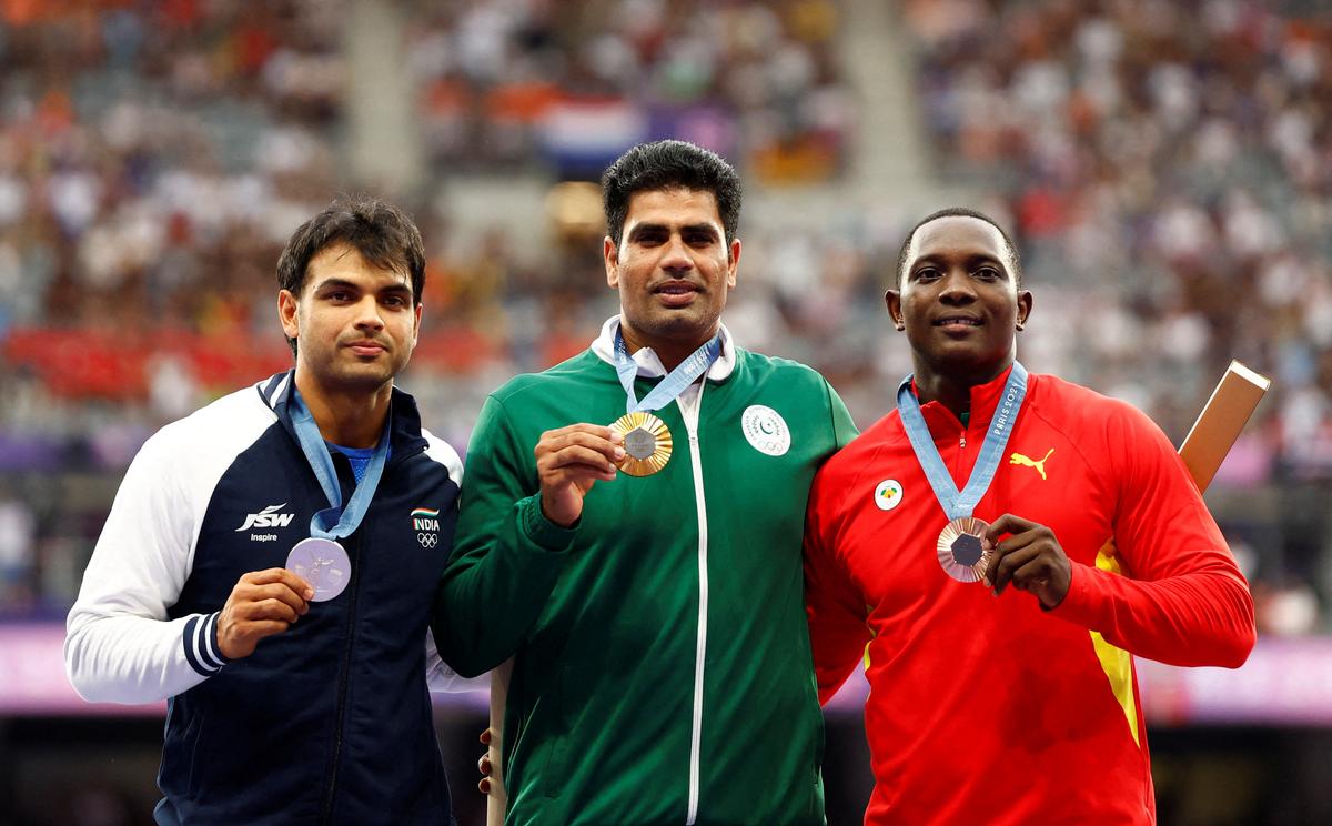 Arshad Nadeem of Pakistan celebrates with his medal on the podium with Silver medallist Neeraj Chopra of India and Bronze medallist Anderson Peters of Grenada.