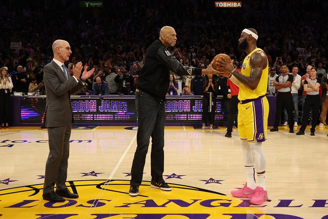 NBA Commissioner Adam Silver looks on as Kareem Abdul-Jabbar ceremoniously hands LeBron James the ball after James passed Abdul-Jabbar to become the NBA’s all-time leading scorer.