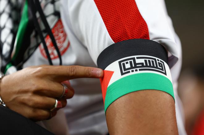 A Morocco fan points to his armband displaying the flag of Palestine, inside the stadium before the match.