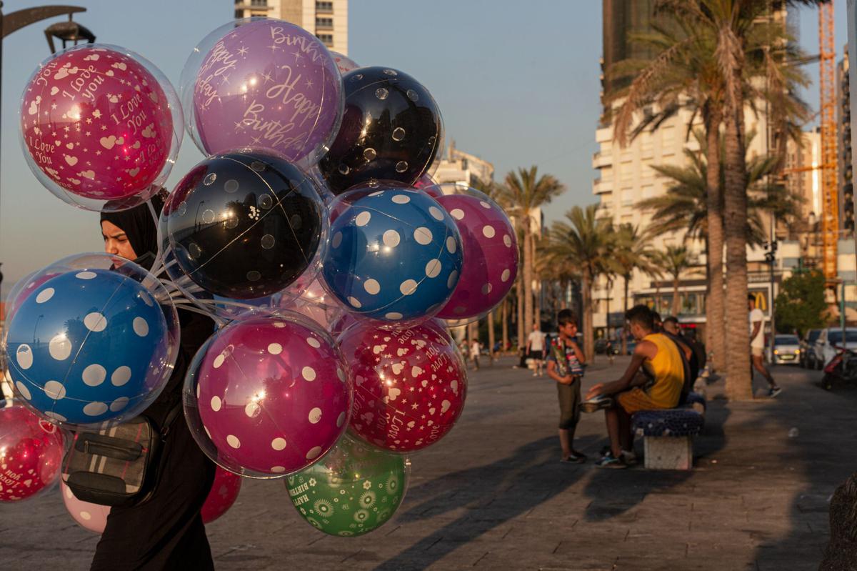 Making a Living: A woman sells balloons as children sell roses in Beirut on August 13, 2021.