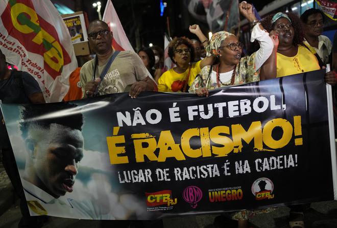 People hold a banner that reads in Portuguese; “It isn’t football, it is racism” during a protest against racism suffered by Brazilian Vinicius.