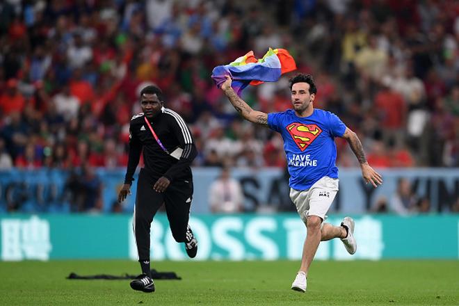 A pitch invader wearing a shirt reading “Save Ukraine” holds a rainbow flag.