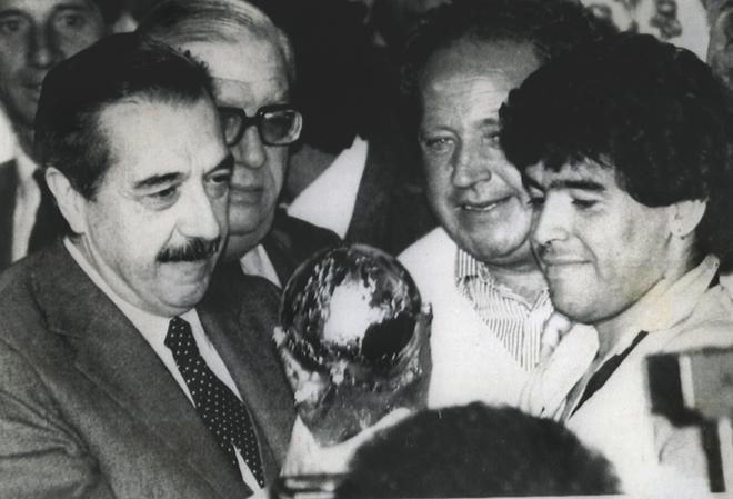 Diego Maradona arată trofeul Cupei Mondiale FIFA 1986 președintelui de atunci al Argentinei Raul Alfonsin la palatul prezidențial din Buenos Aires, Argentina, 3 iulie 1986.  
