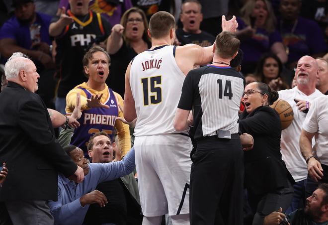 Jokic (15) reaches for the basketball after pushing off Phoenix Suns owner Mat Ishbia (L) during the first half.