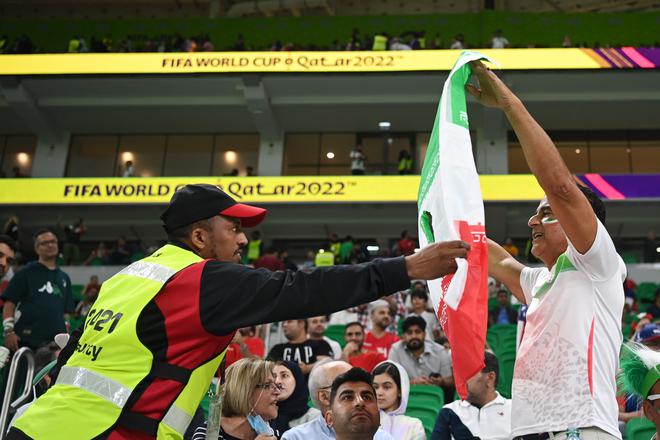 A security staff asks a fan to remove the Iran flag which had its emblem cut off. 