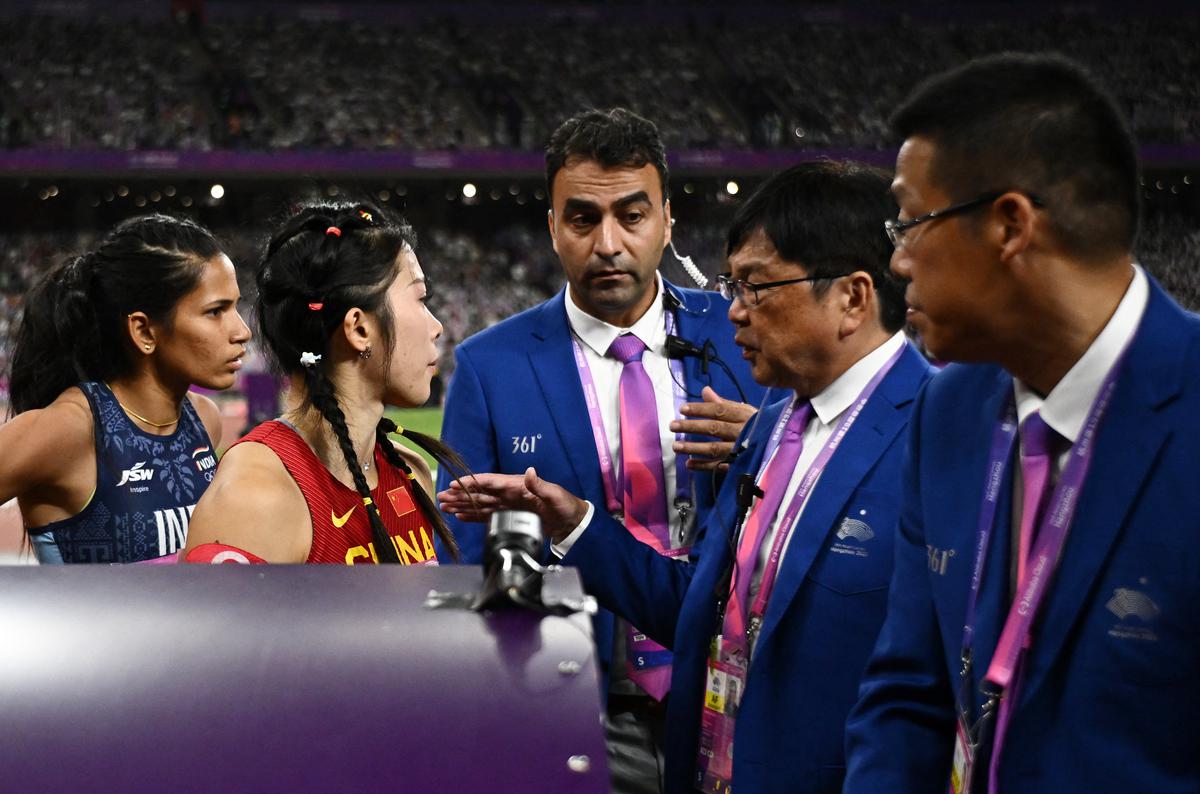 Officials speak to China’s Yanni Wu following a false start in the women’s 100m hurdles final as India’s Jyothi Yarraji looks on.
